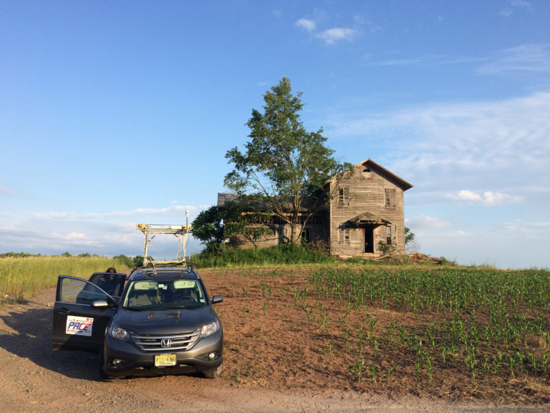 car on a hill next to an abandoned farm house