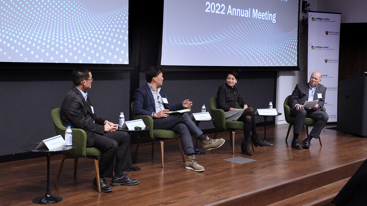 A panel of 3 men and 1 woman take the stage in green seats.