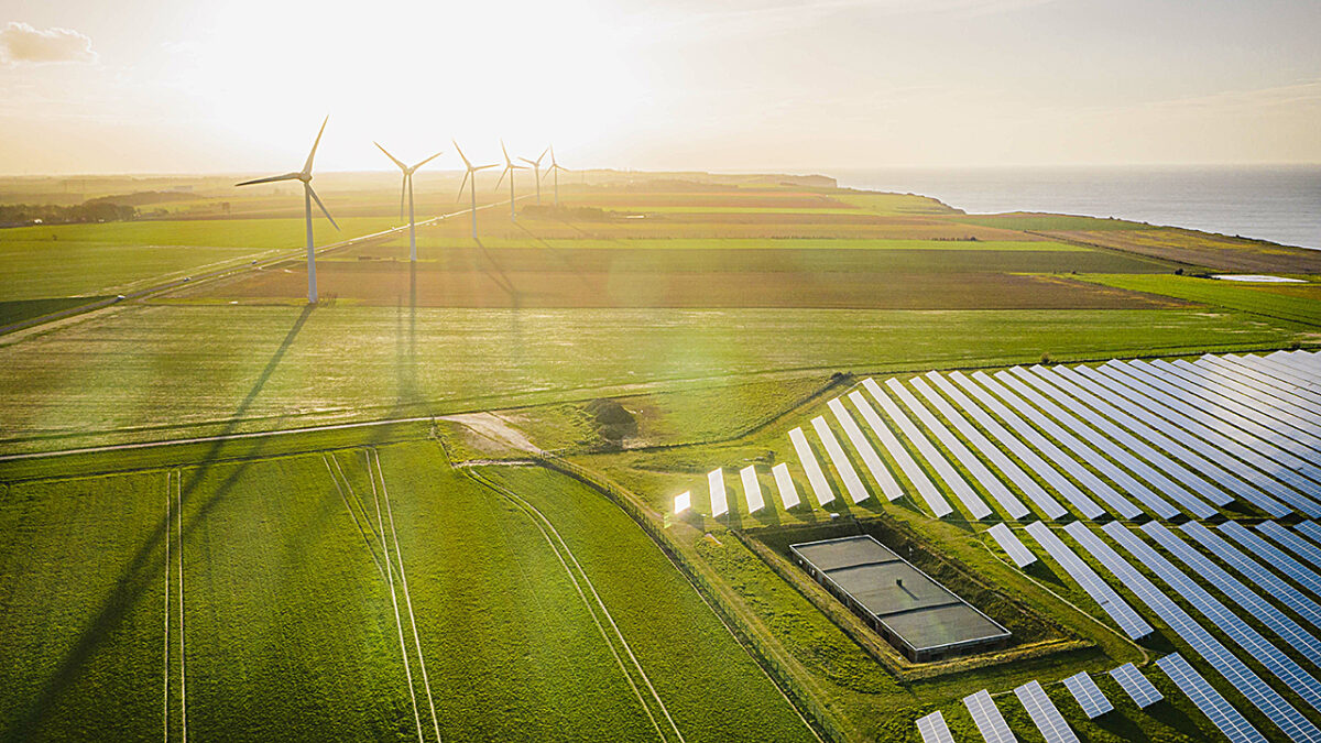 Aerial view of a sunrise over green fields with wind turbines on the left and solar panels on the right.