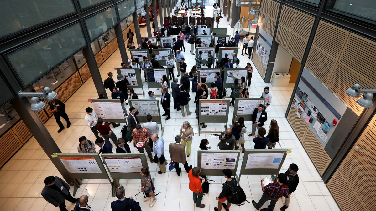 An overhead perspective shot of bulletin boards and people interacting with each other in a large hallway. 