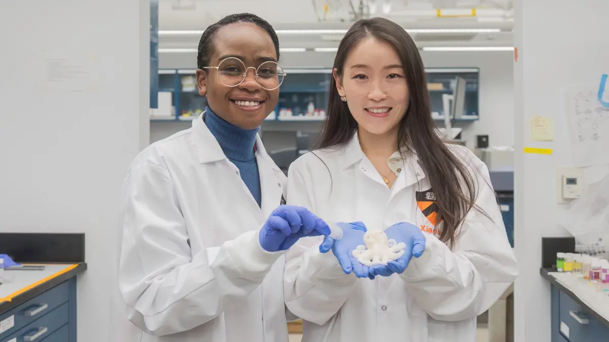 Two women in lab coats hold a hydrogel shaped like a cartoon octopus.