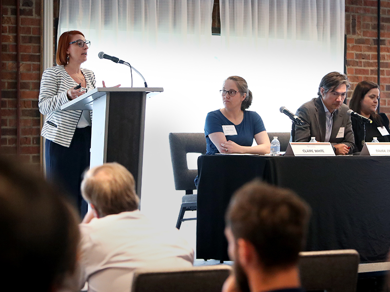 A woman speaks at a podium while other panelists listen