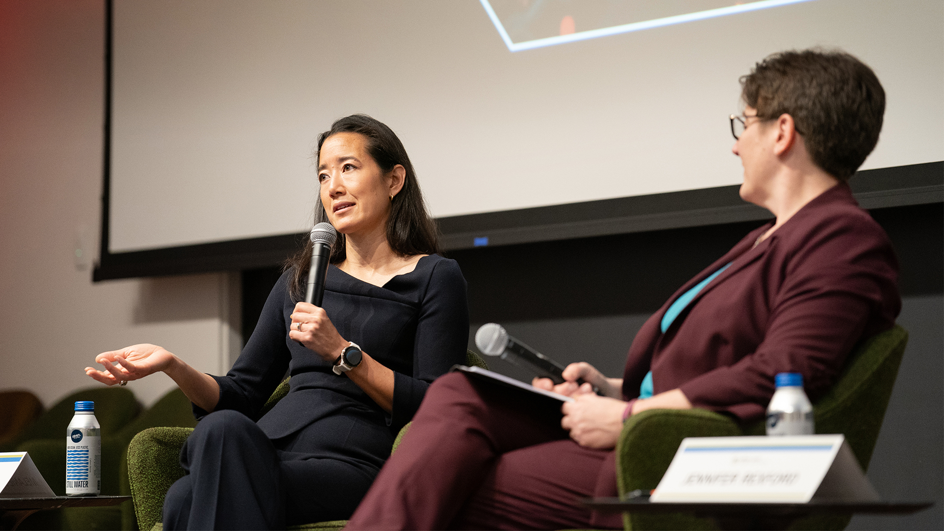 Two women sit on a stage with microphones.