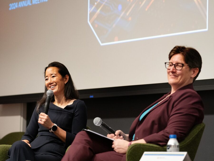 Two women sit on stage, one holding a microphone.