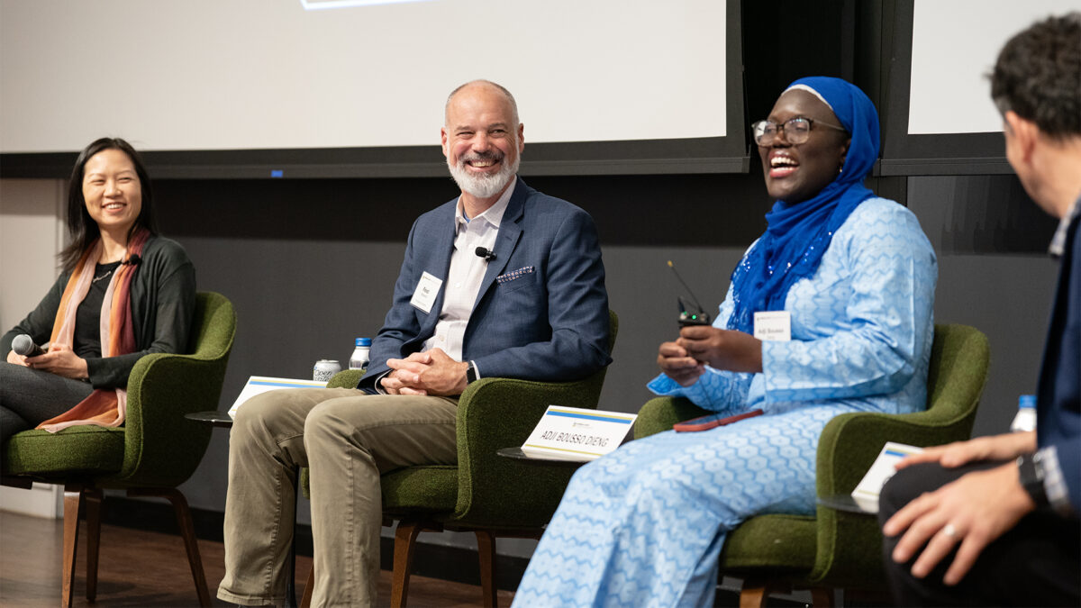 A man in the center of the stage laughs as two women and one man beside him look on.