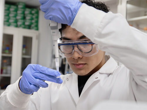 A man standing in a biology lab using a pipette.
