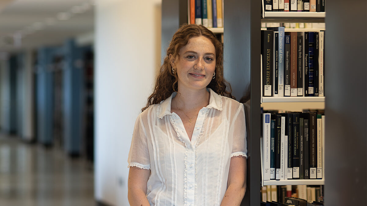 Young woman in a white blouse leaning against a shlef of books in a library