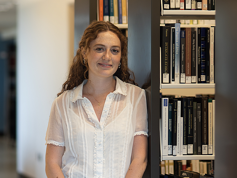 Young woman in a white blouse leaning against a shlef of books in a library
