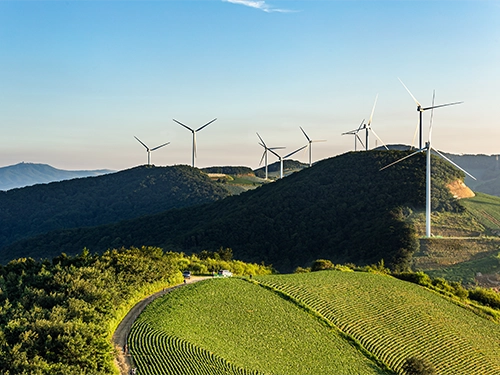 A landscape view of green fields with wind turbines atop hills.