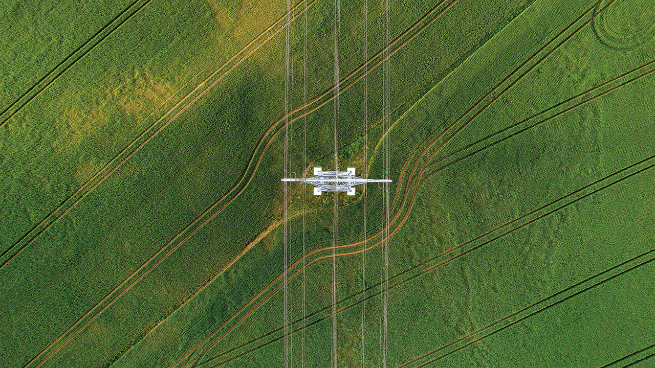 aerial view of a power line tower alone in a green field