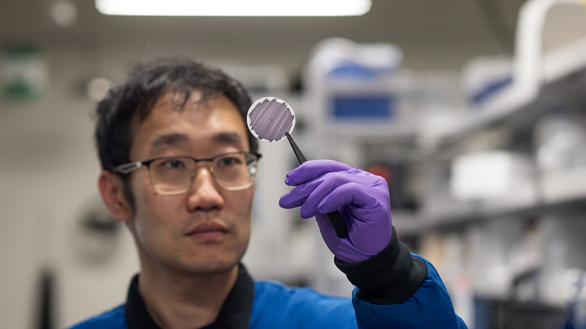 A researcher holds up and examines a thin circular membrane using tweezers.