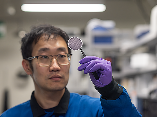 A researcher holds up and examines a thin circular membrane using tweezers.