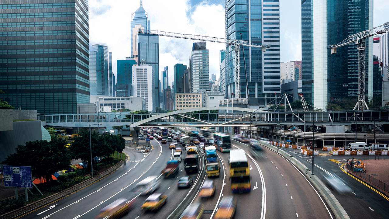 Cars and buses wind down a highway from an urban center
