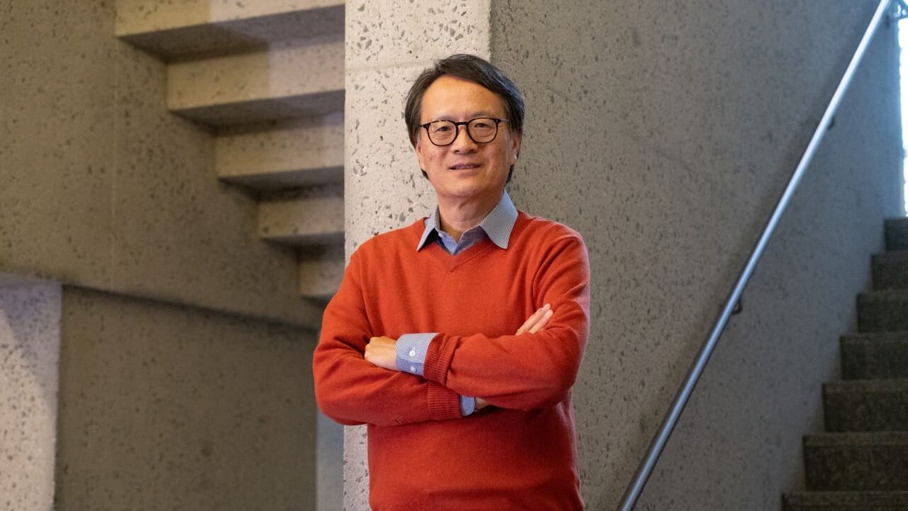 A man in an orange sweater poses in front of a granite wall.