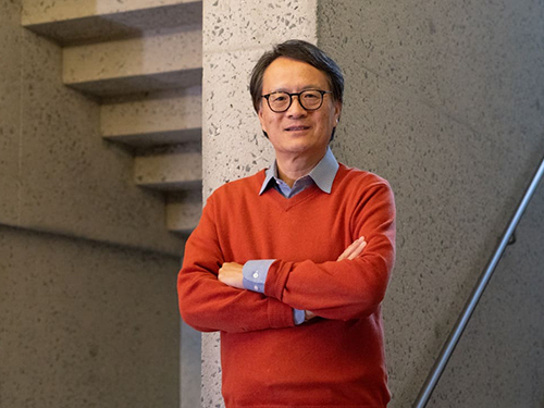 A man in an orange sweater poses in front of a granite wall.