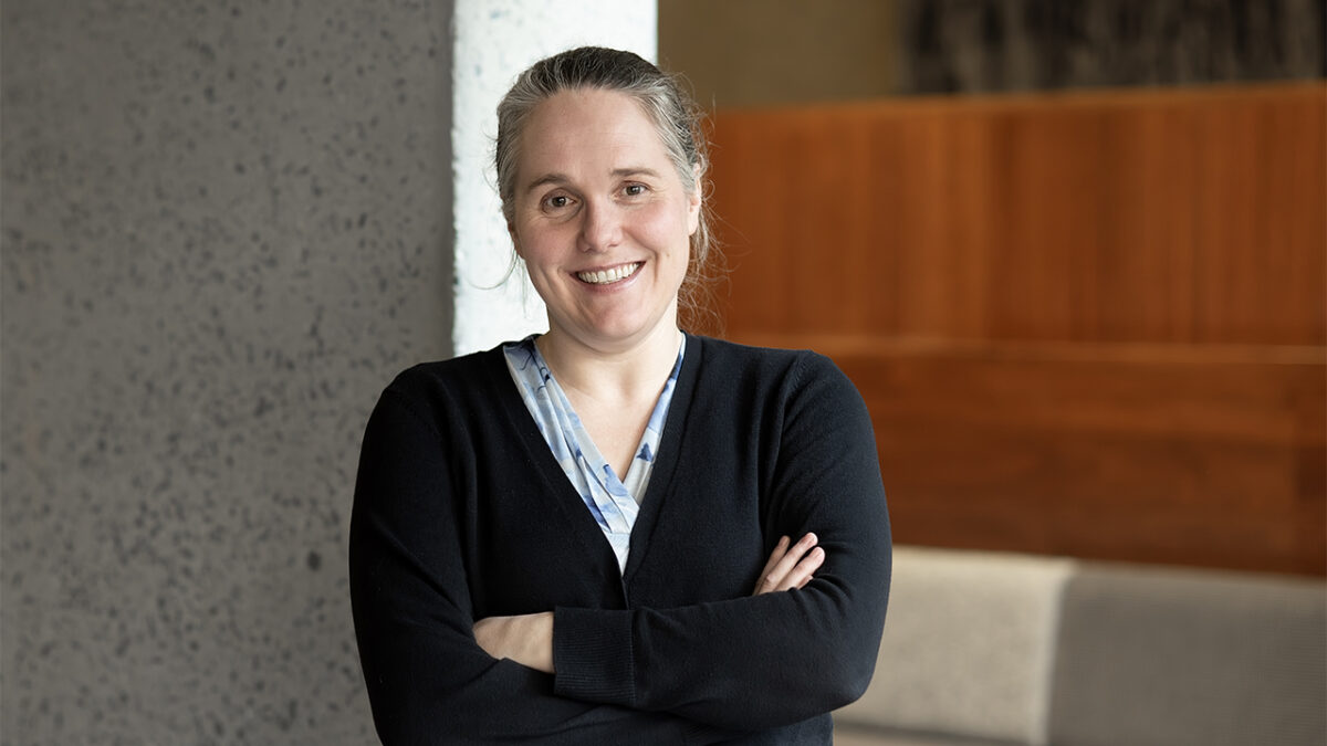 A woman stands with her arms crossed in a modern lobby setting.