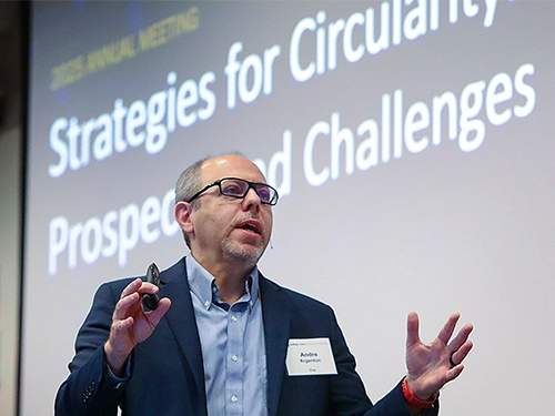 A speaker in a suit gestures passionately during a presentation on "Strategies for Circularity." The presentation is titled "Prospects and Challenges."