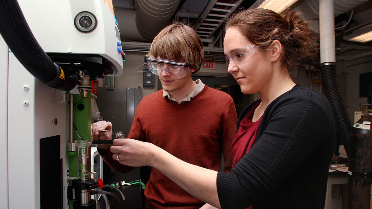 Two scientists in safety goggles work intently with lab equipment in an industrial lab setting.
