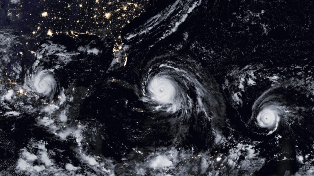 Satellite image showing three hurricanes in the Atlantic Ocean at night. The storms' swirling eye formations contrast with city lights on the U.S. coast.