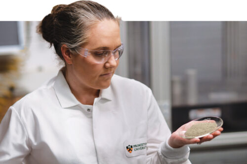 Woman in lab coat examines a glass dish with cement powder