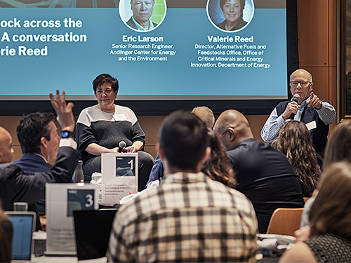 Audience attending a conference on biomanufacturing with speakers Eric Larson and Valerie Reed featured on a screen.
