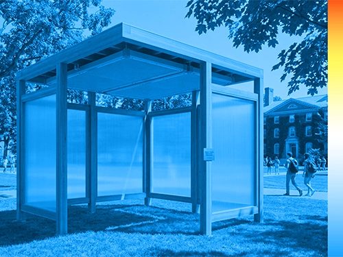 A cube-shaped outdoor structure with translucent walls and a wooden frame is set in a grassy park.