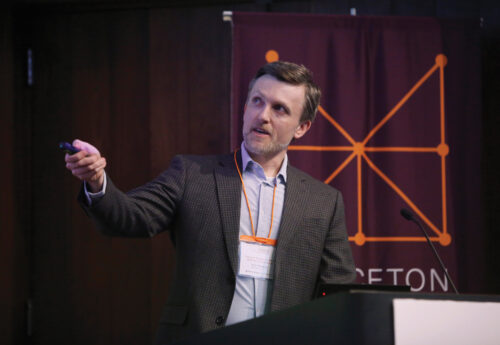 A man on a stage gestures to his left.