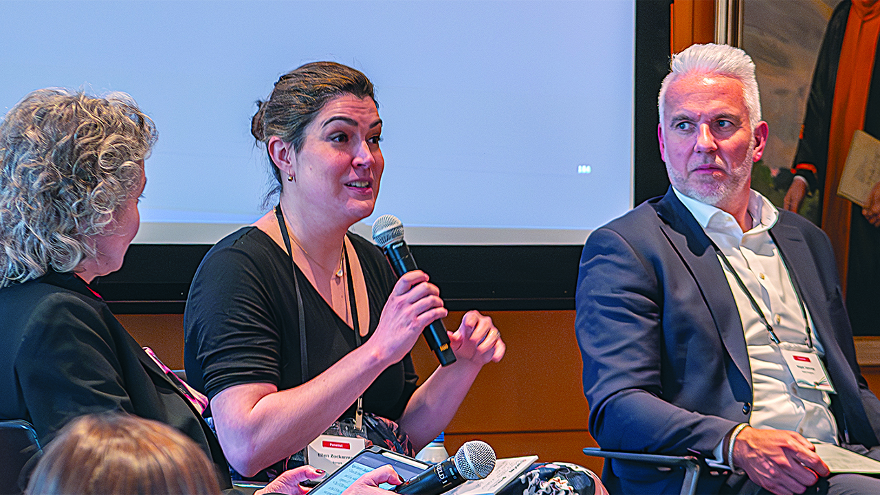 A woman speaks to a mic while two others look on.