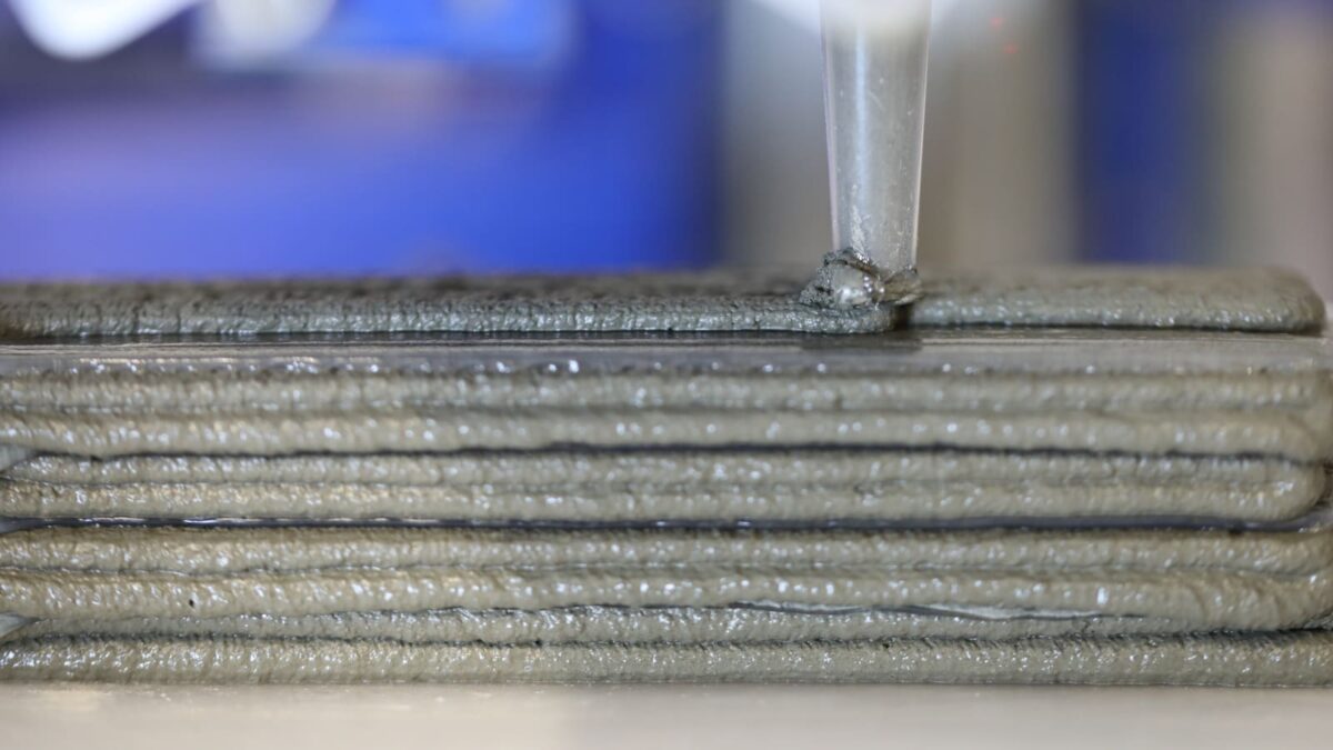 A close up of a nozzle adding a metallic silvery-grey layer upon others.