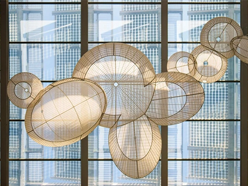 Hanging installation of large, woven, circular structures casting intricate shadows against a tall glass building.