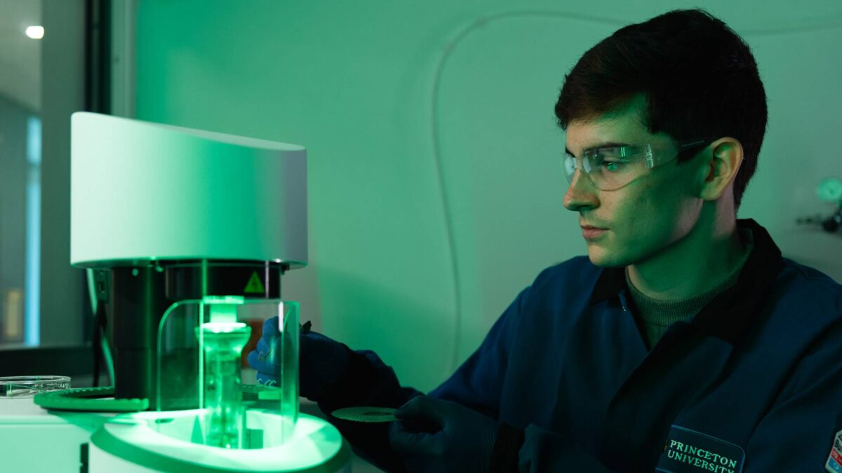 A male researcher handles glass and machinery in a room illuminated in green light.