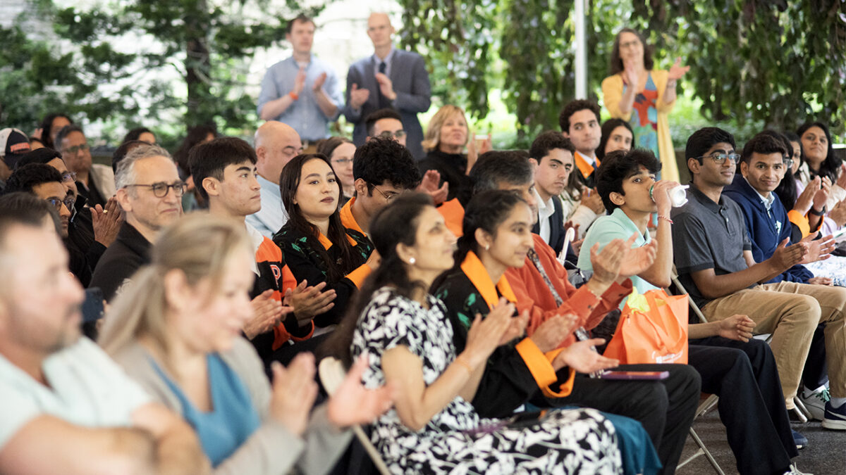 A crowd clapping and seated under an outdoor tent.