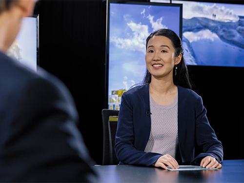 Woman sits behind a television anchor's table.